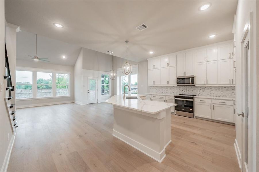 Kitchen with appliances with stainless steel finishes, backsplash, white cabinetry, a chandelier, and hanging light fixtures