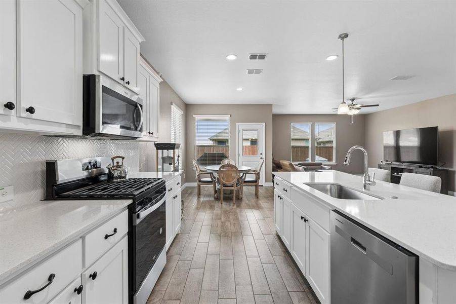 Contemporary kitchen featuring white cabinetry, stainless steel appliances, light-toned countertops, and wood-finish flooring