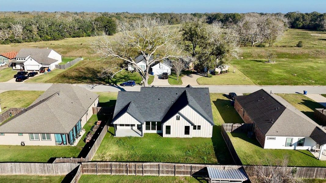 This aerial photo showcases a charming suburban home with a modern design, featuring a spacious backyard enclosed by a privacy wooden fence. Surrounded by well-maintained neighboring houses, it's situated in a quiet, area with ample open space nearby, offering a peaceful environment.