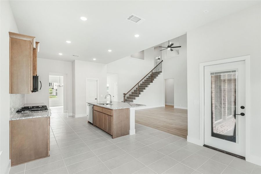 Open-concept kitchen with center island, granite countertops, and tile floors, open to living area with staircase