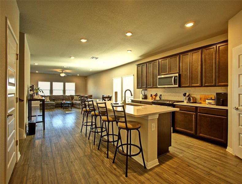 Kitchen with a center island with sink, a kitchen breakfast bar, stainless steel appliances, open floor plan, and dark wood finished floors Kitchen with a center island with sink, a kitchen breakfast bar, stainless steel appliances, open floor plan, and dark wood finished floors