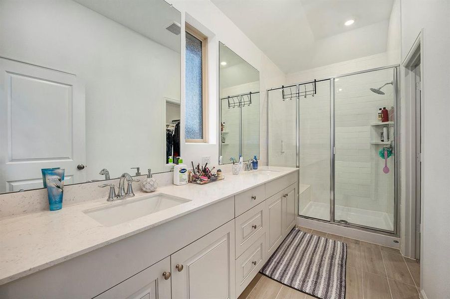 This bathroom features a spacious layout with a large double vanity and ample counter space. It includes a glass-enclosed shower with modern fixtures and a sleek, tiled floor. The neutral color palette and well-placed lighting create a bright and inviting atmosphere.