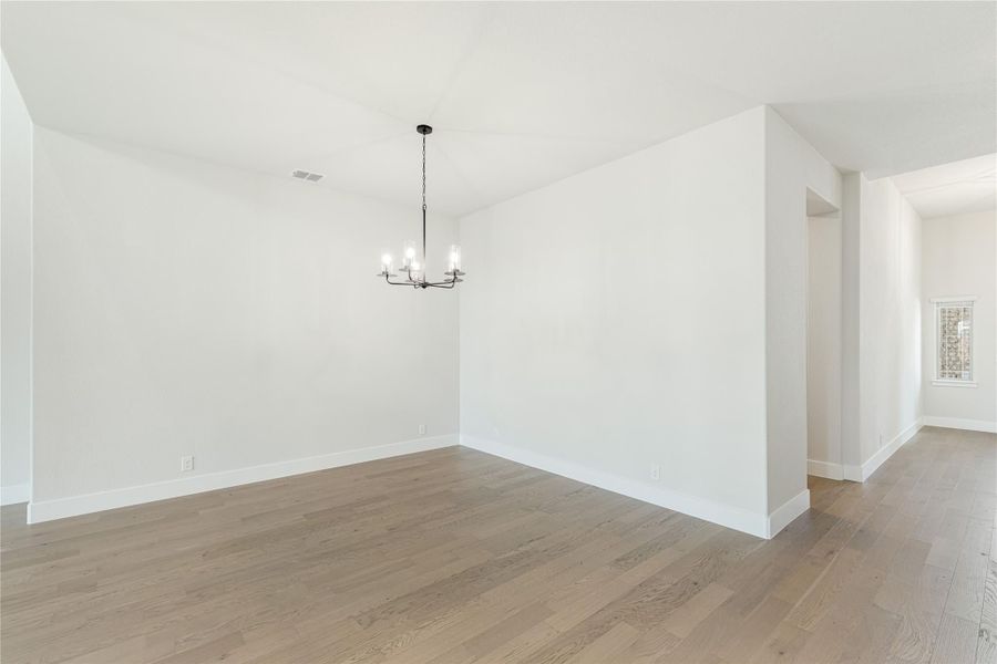 Empty dining room with hardwood floors, white walls, and a black chandelier overhead Empty dining room with hardwood floors, white walls, and a black chandelier overhead