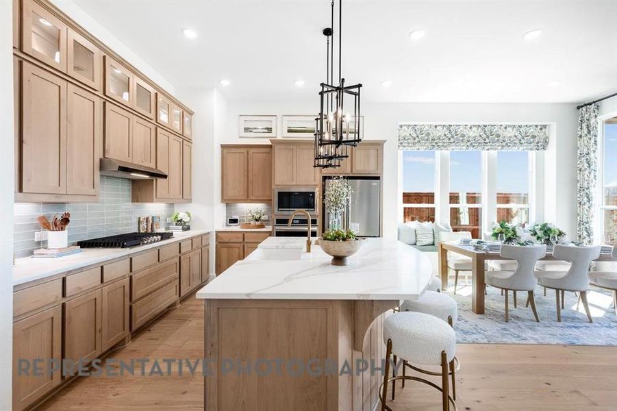 Kitchen with backsplash, a breakfast bar area, an island with sink, light wood-style flooring, and light stone counters