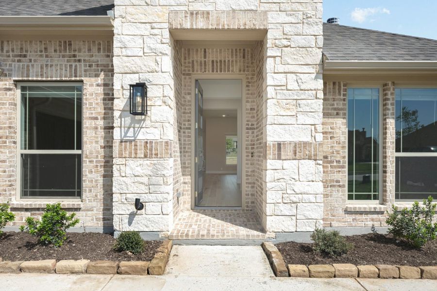 Home entrance with light brick and stone exterior, open front door, black wall lantern, and brick walkway.