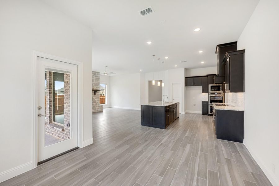 Open-concept kitchen and living area with dark cabinets, center island, stainless appliances, and light wood-look tile floors. Open-concept kitchen and living area with dark cabinets, center island, stainless appliances, and light wood-look tile floors.