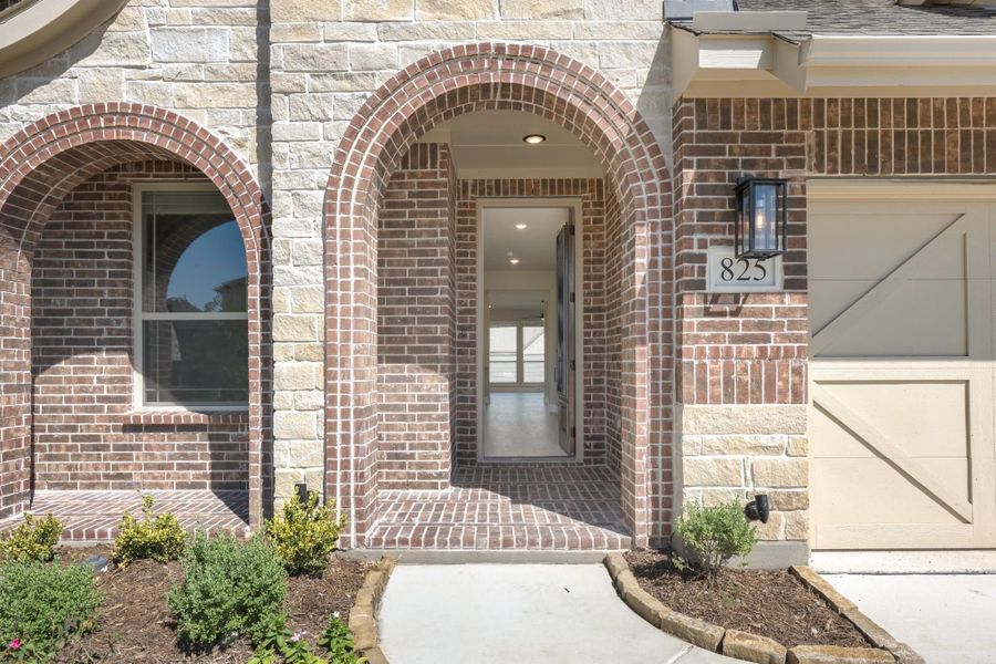 Home entrance with brick arched doorway, stone exterior, house number 825, and attached garage door