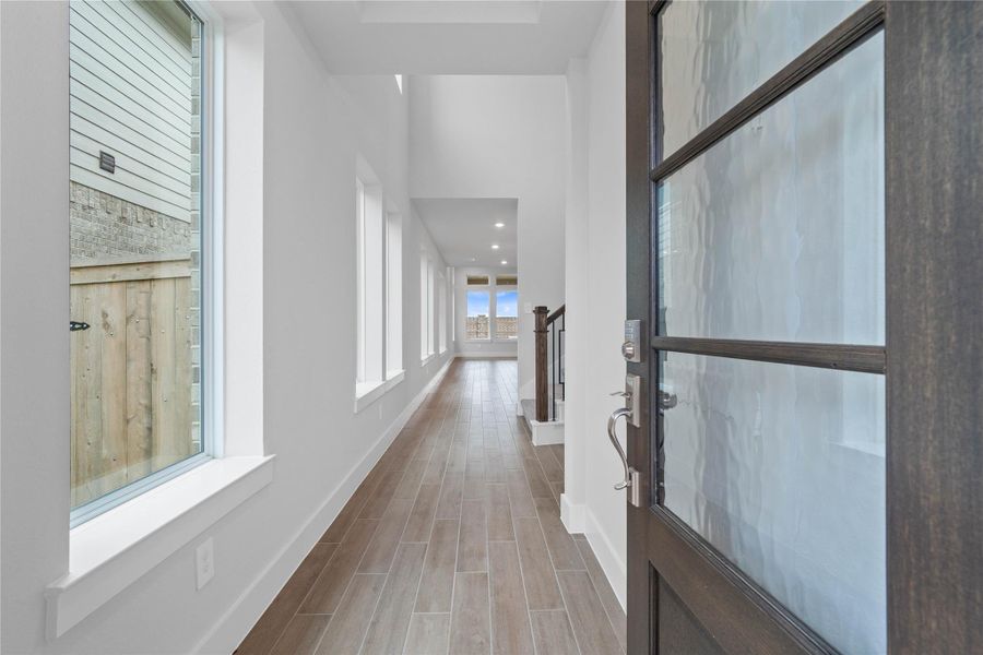 Step inside to a bright interior entryway. The space is accentuated by high, vaulted ceilings and gorgeous wood tile flooring. The hallway extends toward large windows at the rear, flooding the area with natural light.