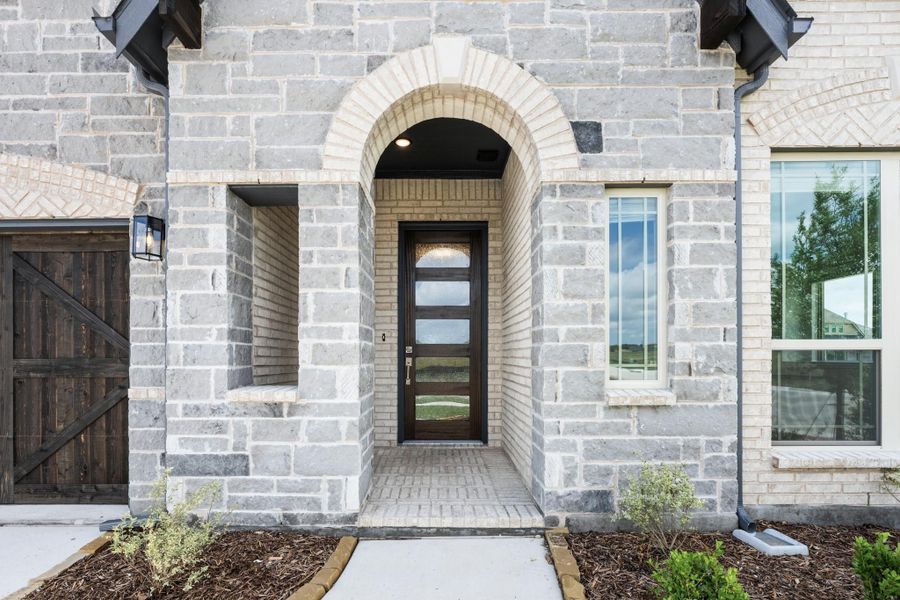 Stone home entrance with arched doorway, dark wood front door with glass panels, and brick exterior.