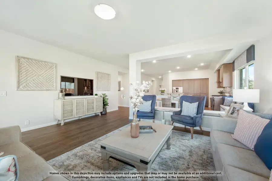 Open-concept living room with hardwood floors, gray sofa, and blue accent chairs, open to kitchen beyond
