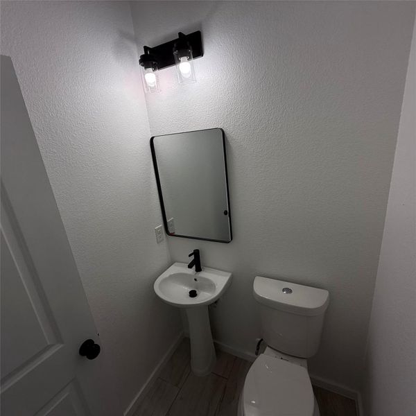 Pedestal sink with a matte black faucet, complemented by a rectangular framed mirror and a two-bulb vanity light fixture
