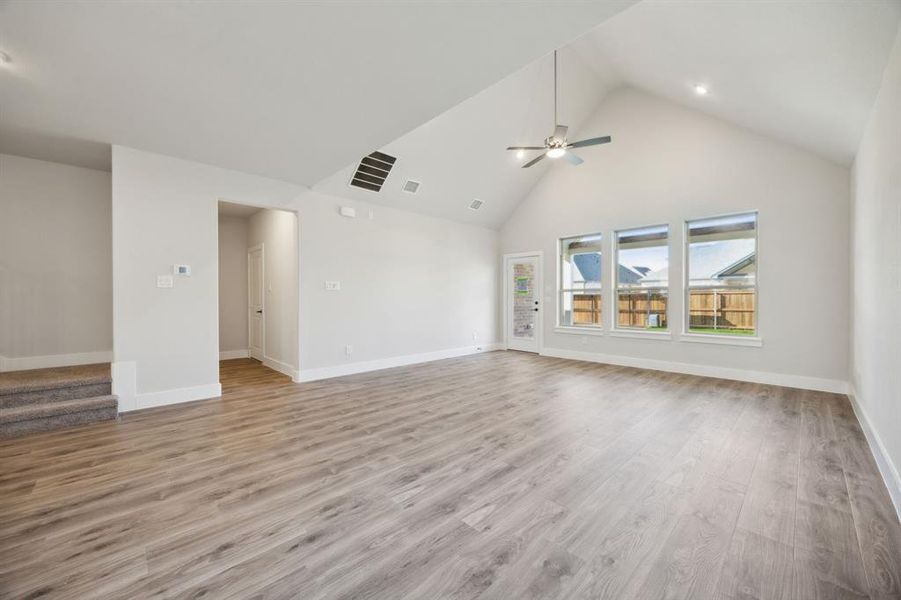 Unfurnished living room with ceiling fan, light wood-type flooring, and high vaulted ceiling