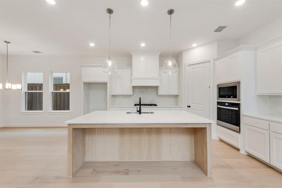 Kitchen with light stone counters, stainless steel appliances, hanging light fixtures, white cabinets, and recessed lighting Kitchen with light stone counters, stainless steel appliances, hanging light fixtures, white cabinets, and recessed lighting