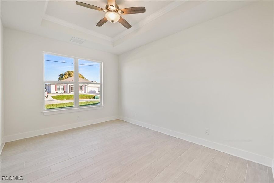 Unfurnished room featuring light wood-style flooring, a tray ceiling, crown molding, and ceiling fan
