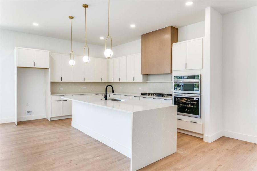 Kitchen with backsplash, light countertops, a center island with sink, light wood-style flooring, and white cabinetry Kitchen with backsplash, light countertops, a center island with sink, light wood-style flooring, and white cabinetry