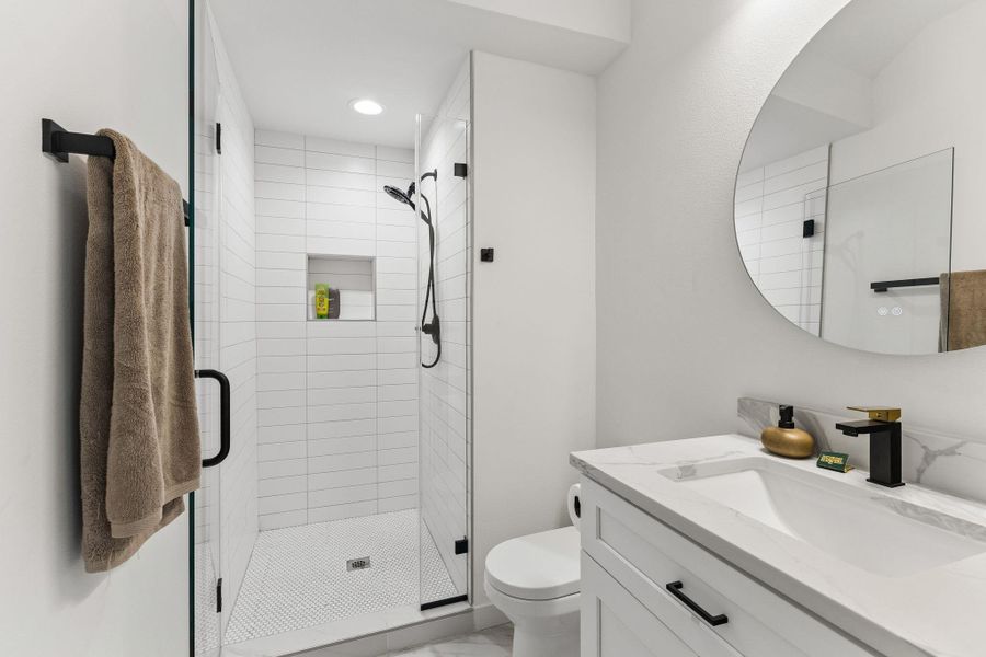 Modern bathroom featuring a glass-enclosed shower with white subway tile, a built-in shower niche, and a contrasting black showerhead