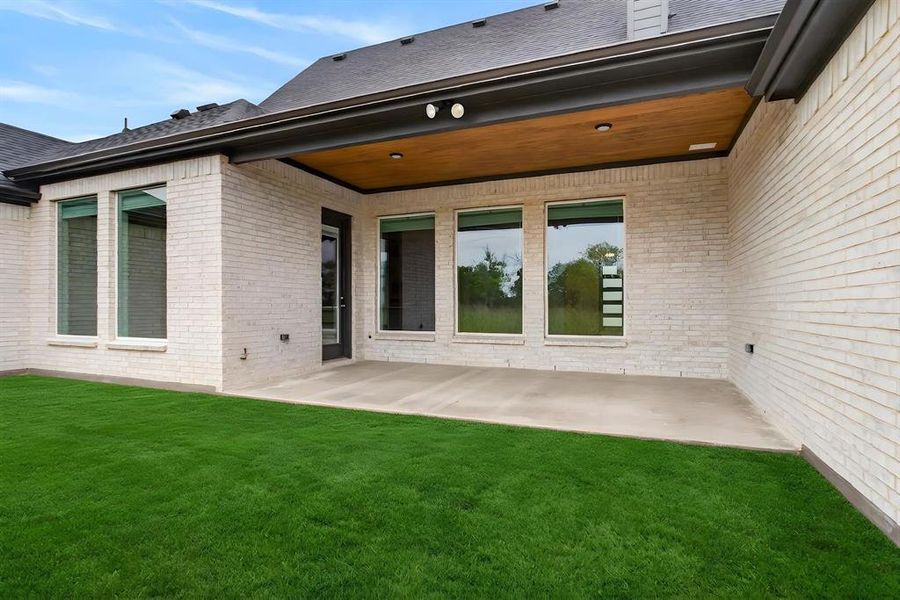 Rear exterior featuring a covered patio with a wood-finish ceiling and recessed lighting, light-colored brick facade, multiple large windows, a glass-paned door, and a manicured lawn Rear exterior featuring a covered patio with a wood-finish ceiling and recessed lighting, light-colored brick facade, multiple large windows, a glass-paned door, and a manicured lawn