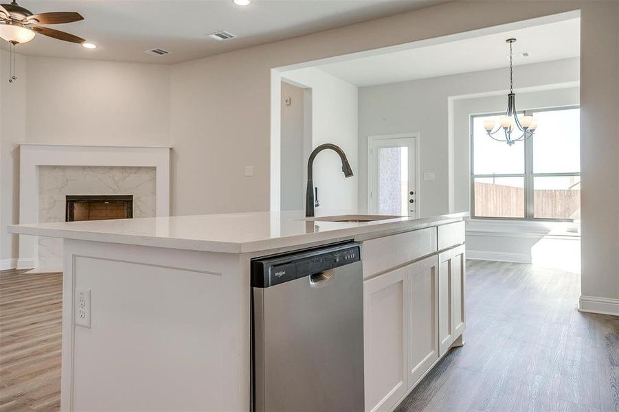 Kitchen with stainless steel dishwasher, sink, white cabinetry, hanging light fixtures, and an island with sink