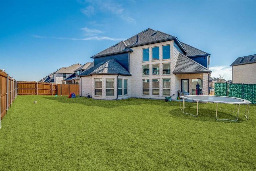 Back of property featuring a lawn and a trampoline