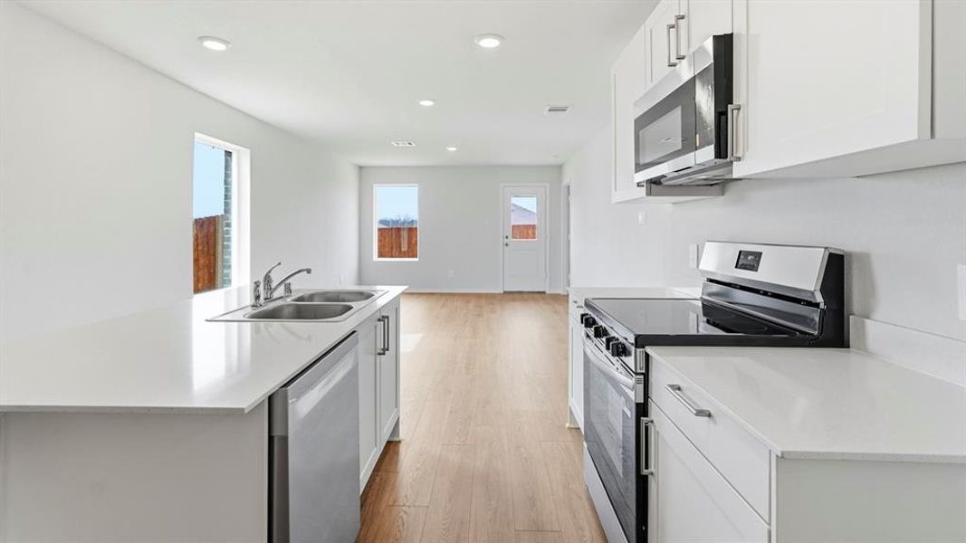 Kitchen with stainless steel appliances, a center island with sink, white cabinets, light wood-type flooring, and recessed lighting