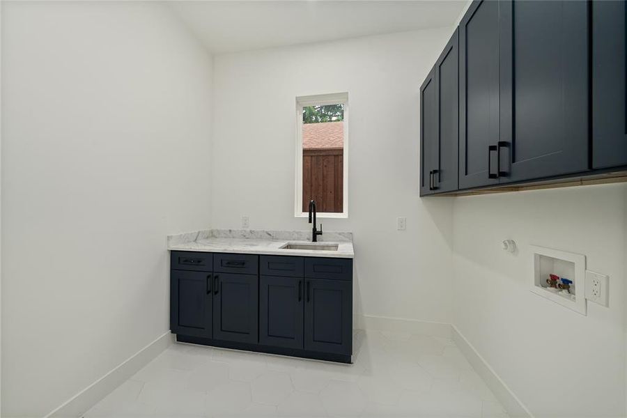 Utility room featuring dark cabinetry with a sink, a window, and white walls