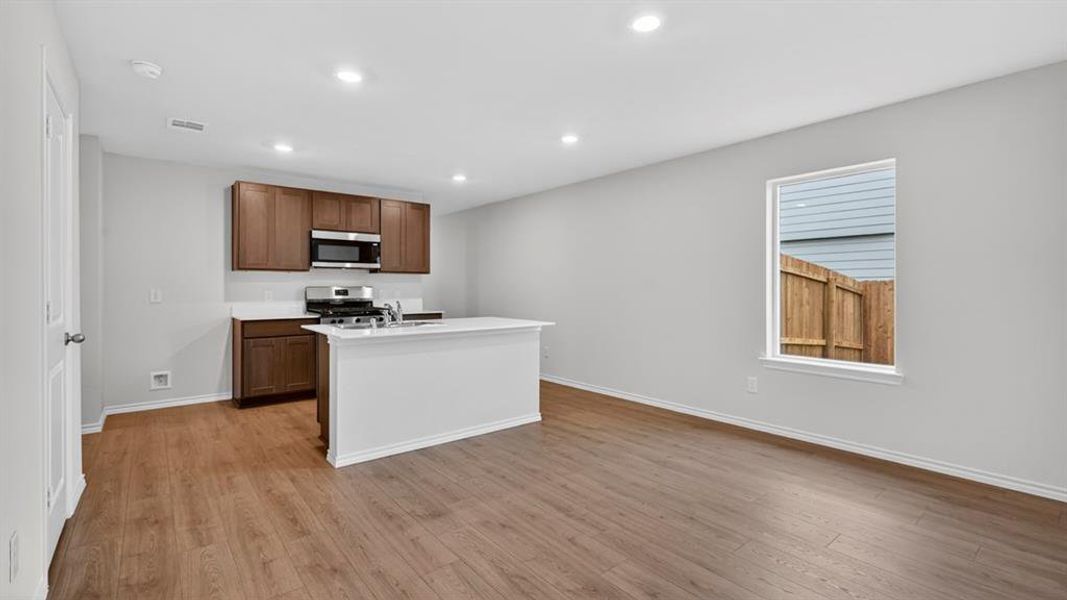 Open-concept living space featuring wood-finish flooring, recessed lighting, and a kitchen island with an integrated sink