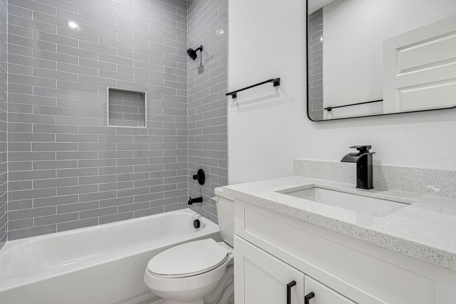 Upstairs hallway bathroom featuring a modern vanity with quartz countertops, matte black fixtures, and a tub/shower combination with gray tile extending to the ceiling for a clean, contemporary finish.