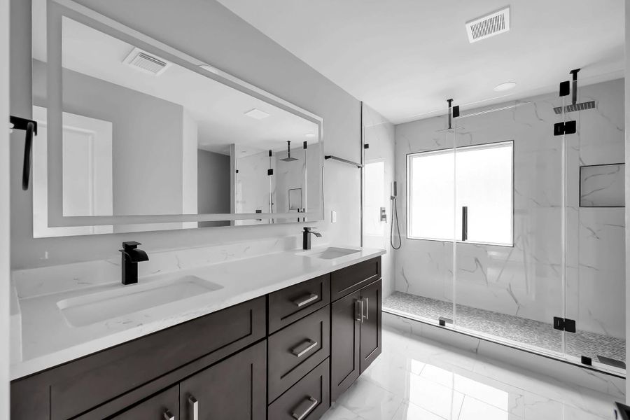 This modern bathroom features a spacious double vanity with sleek black fixtures and ample storage. It includes a large, glass-enclosed shower with elegant tile work and a rainfall showerhead. The room is bright and airy, with a large window allowing natural light to flood in.