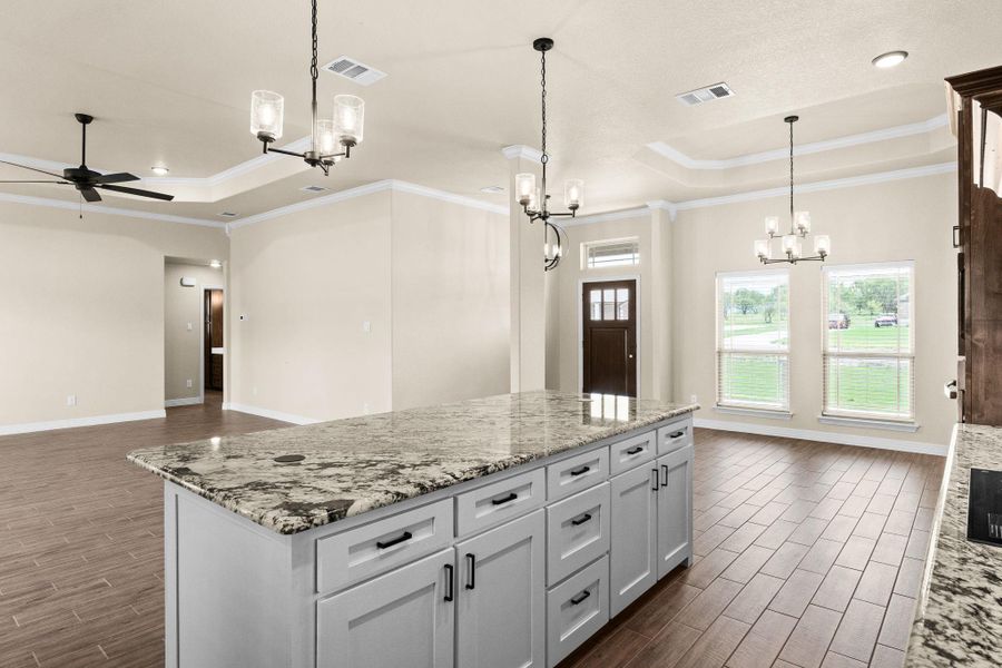 Kitchen with a raised ceiling, light granite countertops, wood like tile floors, open floor plan, and crown molding Kitchen with a raised ceiling, light granite countertops, wood like tile floors, open floor plan, and crown molding