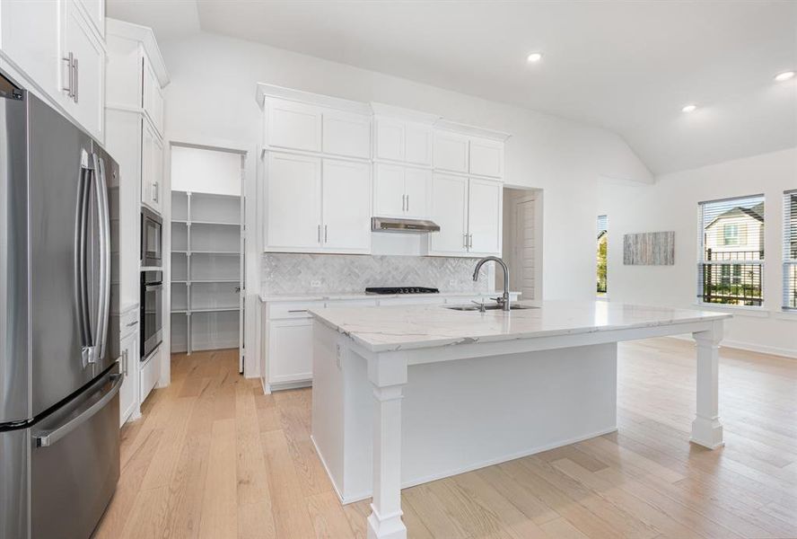 Kitchen featuring stainless steel appliances, lofted ceiling, tasteful backsplash, light stone countertops, and light wood-style floors Kitchen featuring stainless steel appliances, lofted ceiling, tasteful backsplash, light stone countertops, and light wood-style floors