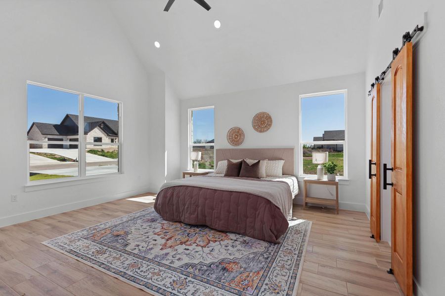 Bedroom featuring a barn door, lofted ceiling, recessed lighting, light wood finished floors, and a ceiling fan Bedroom featuring a barn door, lofted ceiling, recessed lighting, light wood finished floors, and a ceiling fan