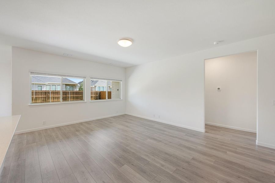 Empty living room with light hardwood floors, white walls, and two windows overlooking a backyard fence. Empty living room with light hardwood floors, white walls, and two windows overlooking a backyard fence.