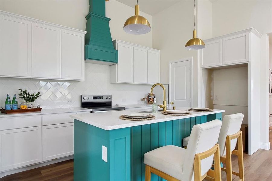 Kitchen with stainless steel range with electric cooktop, white cabinetry, decorative light fixtures, an island with sink, and backsplash