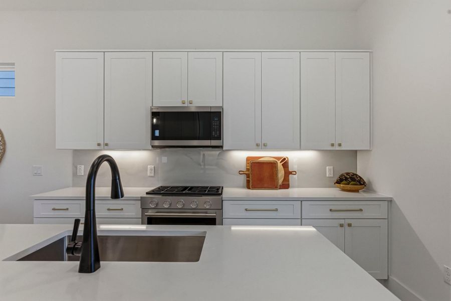 Kitchen with white cabinetry, stainless steel appliances, and light stone counters