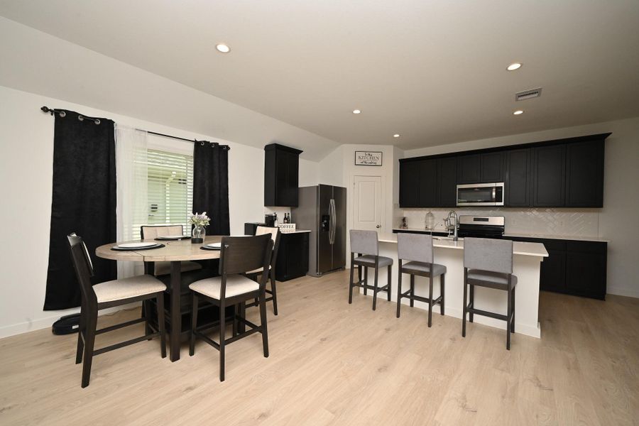 Modern kitchen and dining area with sleek black cabinetry, stainless steel appliances, and light flooring. The space features a center island with bar seating creating an inviting and functional open layout. Modern kitchen and dining area with sleek black cabinetry, stainless steel appliances, and light flooring. The space features a center island with bar seating creating an inviting and functional open layout.