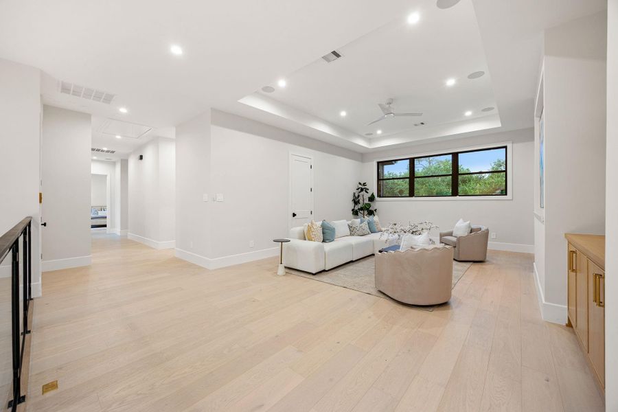 This expansive living area offers a bright, open layout perfect for relaxing or entertaining, with wide-plank flooring and clean modern finishes throughout. Natural light pours in through large windows, creating an inviting atmosphere. The highlight of this room is the tray ceiling with recessed lighting, adding depth, dimension, and a sophisticated architectural element to the space.