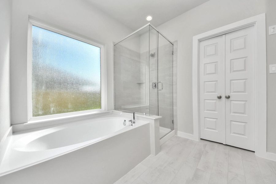 Indulge in a spa-like retreat within the confines of this primary bathroom. Delight in a spacious walk-in shower enveloped in stylish tile surround, unwind in a separate garden tub adorned with custom detailing. Sample photo of completed home with similar floor plan. Actual colors and selections may vary.