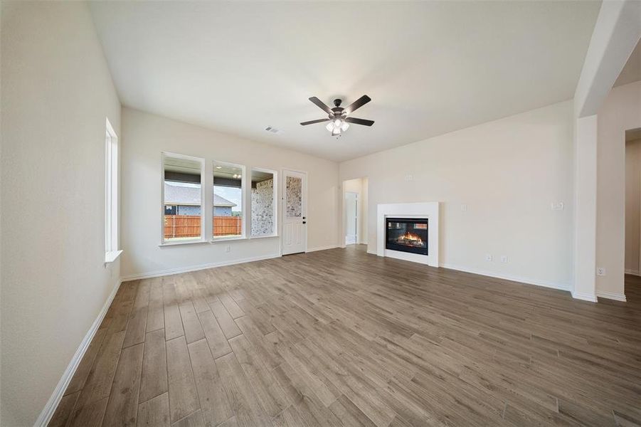 Unfurnished living room featuring wood finished floors, ceiling fan, and a glass covered fireplace
