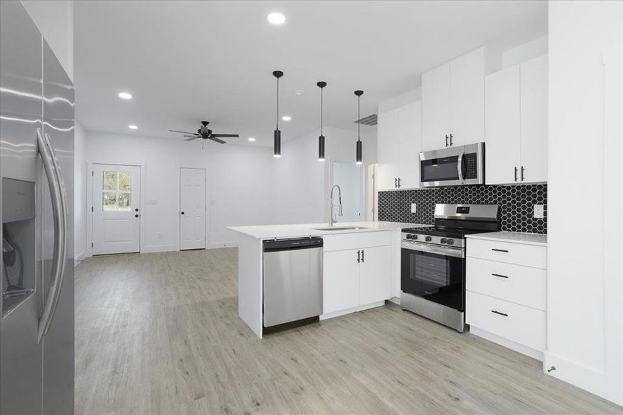 Kitchen featuring kitchen peninsula, light wood-type flooring, stainless steel appliances, sink, and pendant lighting