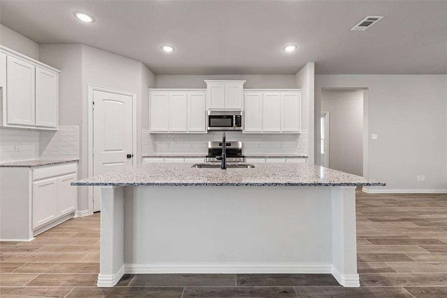Kitchen featuring light stone counters, white cabinetry, backsplash, and recessed lighting Kitchen featuring light stone counters, white cabinetry, backsplash, and recessed lighting