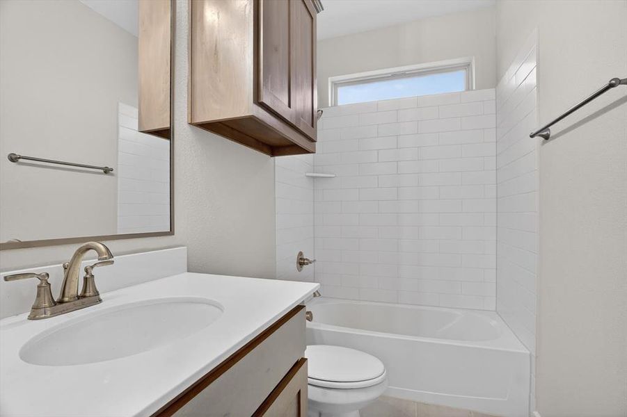 Bathroom featuring a white bathtub with subway tile surround, single vanity with integrated sink, brushed nickel faucet, and wood-finish cabinetry