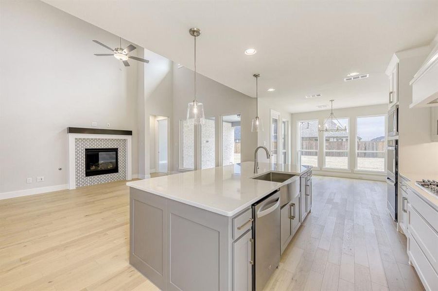Kitchen with a tile fireplace, light wood-type flooring, open floor plan, a center island with sink, and stainless steel appliances