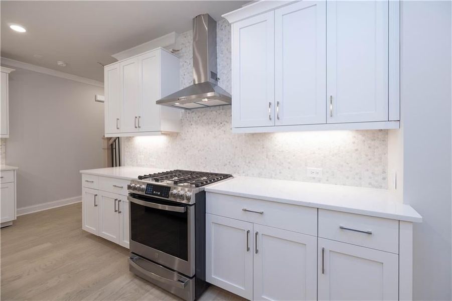 Kitchen with white cabinetry, backsplash, crown molding, gas stove, and wall chimney range hood