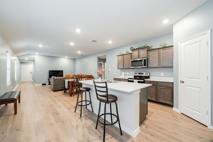 Kitchen featuring stainless steel appliances, light countertops, open floor plan, a kitchen breakfast bar, and a kitchen island with sink Kitchen featuring stainless steel appliances, light countertops, open floor plan, a kitchen breakfast bar, and a kitchen island with sink