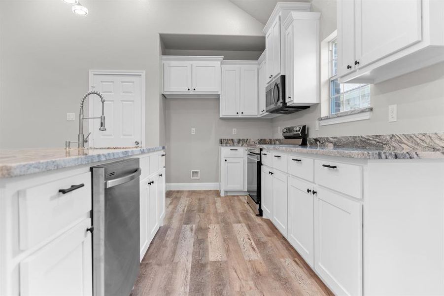 Kitchen featuring stainless steel appliances, a sink, light wood finished floors, white cabinets, and vaulted ceiling Kitchen featuring stainless steel appliances, a sink, light wood finished floors, white cabinets, and vaulted ceiling