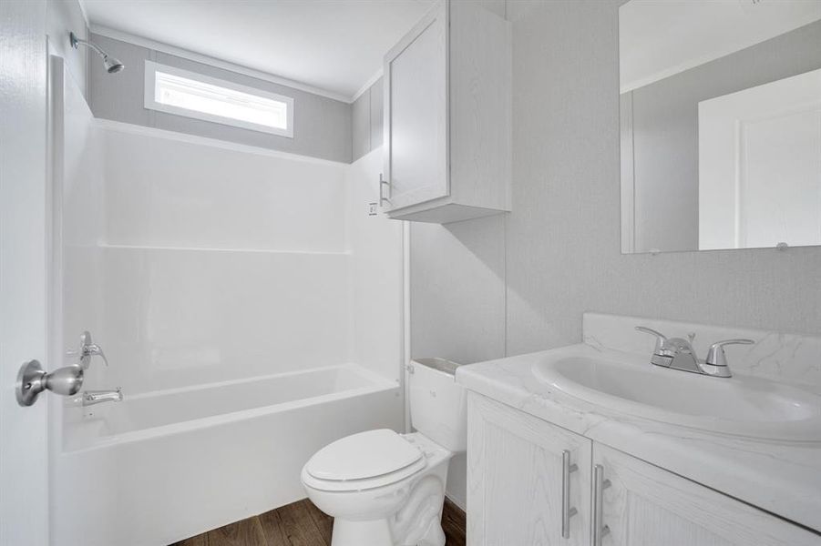 Bathroom featuring a white tub/shower combination with a horizontal window, wood-finish flooring, and a vanity with a white countertop and integrated sink