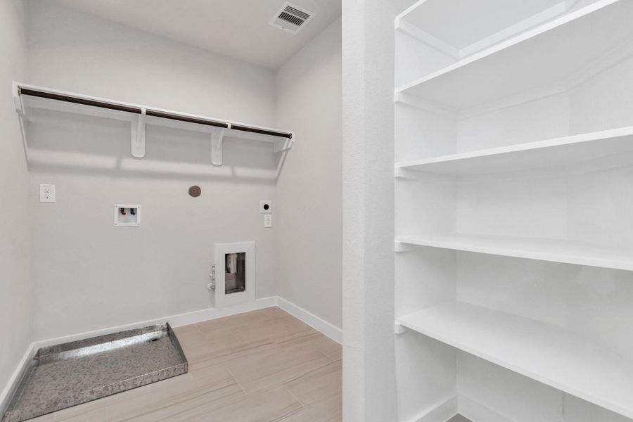 A perfect blend of functionality and comfort. Laundry room, thoughtfully equipped with shelving for effortless organization. Both gas and electric connections available. Sample photo of completed home with similar floor plan. Actual colors and selections may vary.