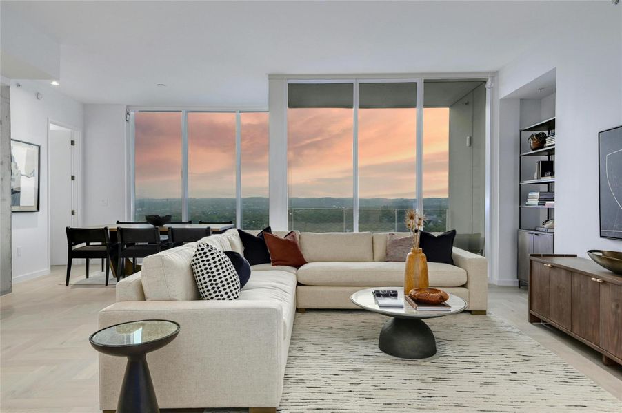 Modern elegance meets breathtaking views in this light-filled living space. Floor-to-ceiling windows frame the stunning Texas Hill Country, while the open-concept design seamlessly connects the living, dining, den and kitchen areas. Neutral tones, sleek finishes, and contemporary furnishings create a sophisticated yet inviting ambiance (Photo from previous model Residence No. 2104 on lower level)
