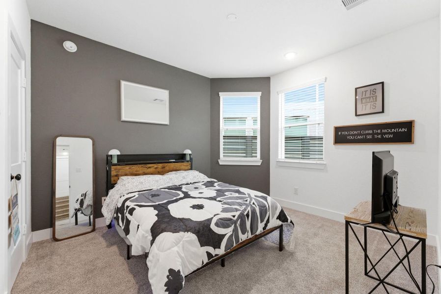 Bright secondary bedroom with large windows, soft carpet, and calming neutral tones.