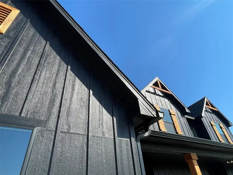 Exterior featuring dark board and batten siding, dark shingle roofing, exposed timber accents, natural wood shutters, and dark gutters